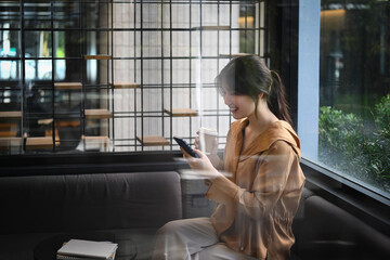 Young businesswoman with takeaway coffee using mobile phone at corporate office break out area