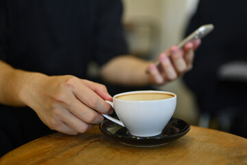 Cropped shot of man hand holding cup of coffee and using mobile phone at cafe
