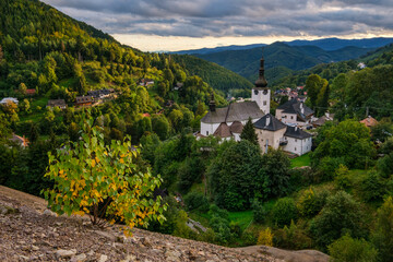 Village Spania Dolina. Fall in Slovakia. Old mining village. Historic church in Spania dolina. Autumn colored trees at sunset. - obrazy, fototapety, plakaty
