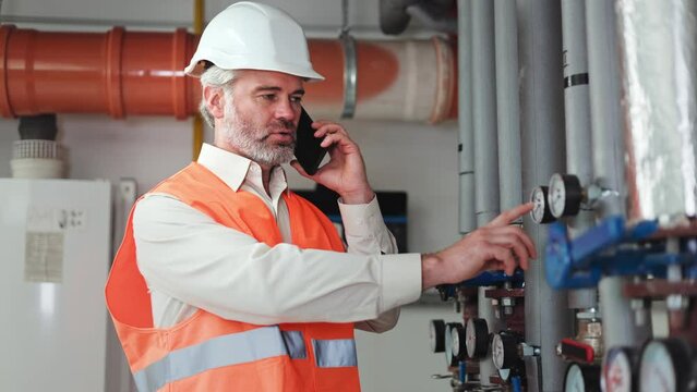 Employee of factory having conversation with director on personal smartphone and telling about indicators on pressure sensors in pipes. Reliable worker reporting about serviceability of equipment.