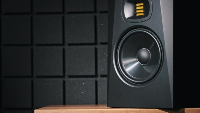 Studio monitor speaker vibrates from bass music in a recording studio, close-up. Modern loudspeaker membrane moves while listening loud song in slow motion. Working bass speaker on low frequency. HiFi