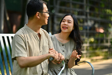 Smiling young woman talking to middle age father and relaxing together on the bench at public park