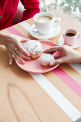 Two Women Holding Pink Jelly Doughnuts Indoors in High Angle View at coffee shop