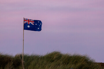 Australian flag flying on a dune at sunset. - 676299536