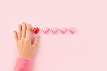 Female hand with pink gel polish manicure and a line of heart shaped candies on pink background