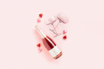A bottle of sparkling wine with two glasses and heart shaped chocolate candies on pink background