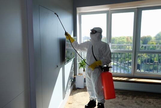 Disinfection to destroy viruses. Worker in protective suit and face mask sprays chemicals indoors concept