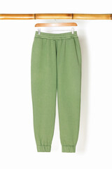 Sweatpants from a green sweatshirt hang on a wooden hanger, front view. The concept of modern comfortable sportswear and detox.