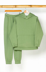 A green sports hoodie and pants hang on a wooden bamboo hanger.
