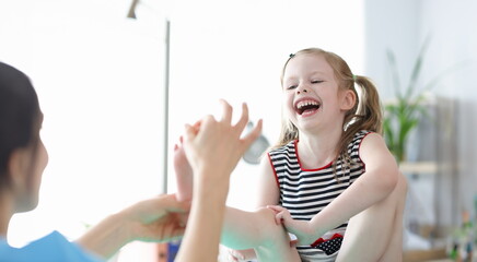 Little laughing girl at doctor appointment showing her foot. Foot massage for children concept - obrazy, fototapety, plakaty