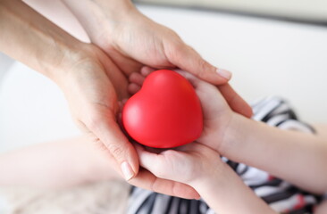 Little girl and mother hands holding red toy heart closeup. Parental love concept
