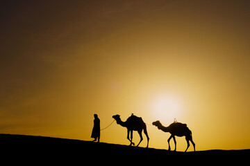 Fototapeta na wymiar Sunrise silhouette of camels and handler, Merzouga