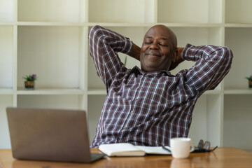 Portrait of an African American senior man sits back in his chair, closing his eyes and enjoying a moment of peace in the office.