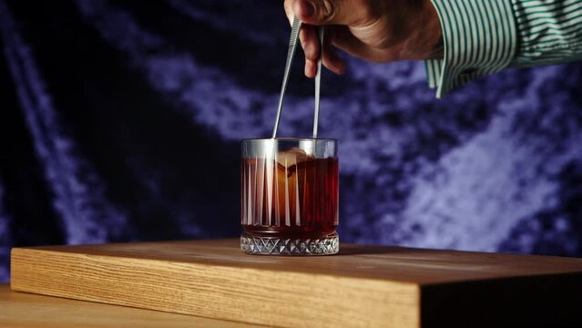 Bartender putting ice cube into negroni cocktail, decorating with dry slice of orange. Gin, sweet vermouth, red bitter liqueur. Concept of cocktails, alcohol drink, bar, taste, menu, pop art style.