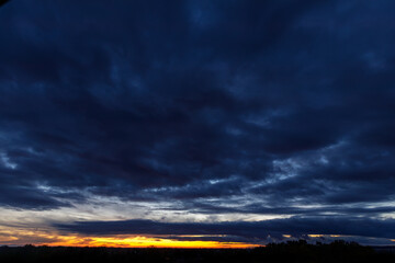 Panoramic sunset sky with heavy dark blue clouds and orange line of sun