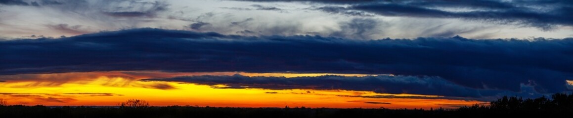 Panoramic sunset sky with heavy dark blue clouds and orange line of sun