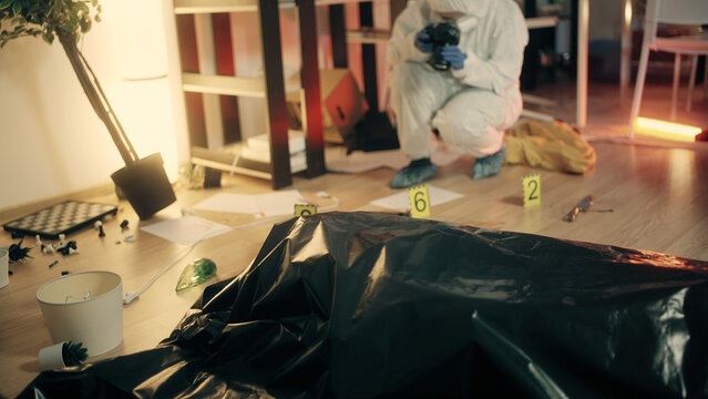 The forensic expert is taking pictures of marked evidence and examining the crime scene with a dead body