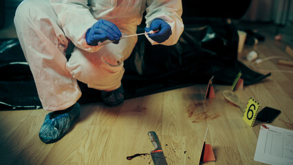 A forensic expert is collecting a blood sample from a marked area with bloodied evidence