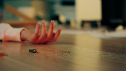 Close-up of a woman lying on the floor after being shot in her apartment, and a bullet casing nearby