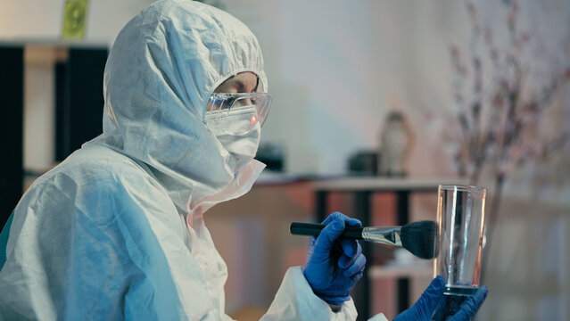 A forensic lab expert is dusting glass for fingerprints and collecting crime evidence