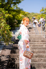 Portrait of a young woman wearing Japanese yukata summer kimono standing on the stone stairs....