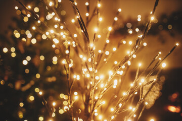 Stylish christmas illuminated tree on background of golden lights bokeh, decorated tree and burning fireplace in evening room. Atmospheric magical christmas eve at fireplace. - obrazy, fototapety, plakaty