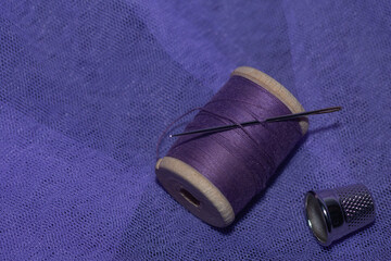 purple threads on a wooden spool with a needle on a background of lilac tulle, thimble.