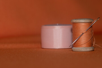 orange  threads on a wooden spool with a needle on a background of orange textile .