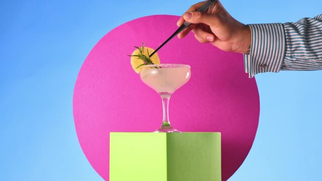 Sweet and sour margarita cocktail over colorful abstract background. Bartender decorating glass with dry pineapple. Concept of cocktails, alcohol drink, bar, taste, menu, pop art style.