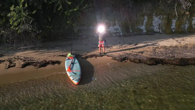 A man on the coast of the sea in a wilderness is signaling for help with a signal mirror