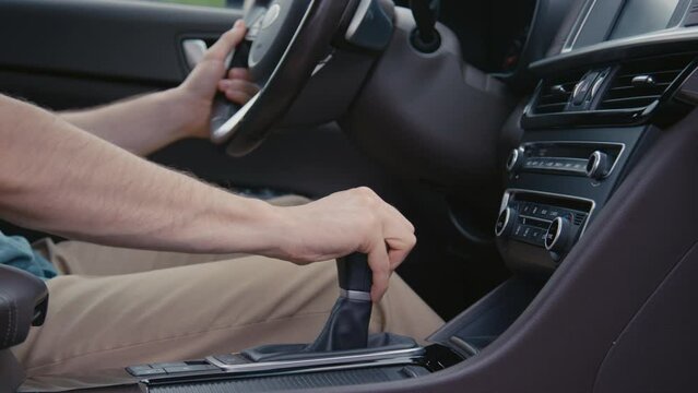 Medium side shot of male drivers hand shifting gear on transmission box while driving a car