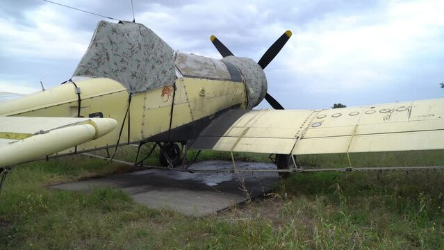 Agriculture yellow coloured aircraft covered with a tarpaulin sheet as a protection from the weather conditions, parked on a grass runaway.
