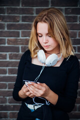 Cute teenage girl with a phone in her hand on the street. A schoolgirl is talking on the phone. Social networking, listening to music with headphones. Youth style.