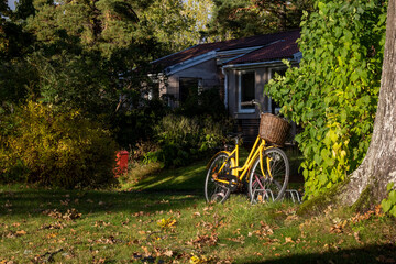Fototapeta na wymiar Yellow bicycle with a wicker basket against the backdrop of village houses on an autumn evening