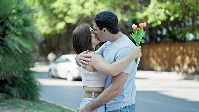 Beautiful couple surprise with bouquet of flowers hugging each other kissing at park