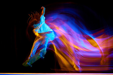 Man skateboarder performing freestyle tricks in motion isolated black background in mixed neon...