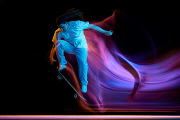 Contemporary extreme kind of sport. Man, skateboarder performing tricks with mixed neon motion blur isolated black background.