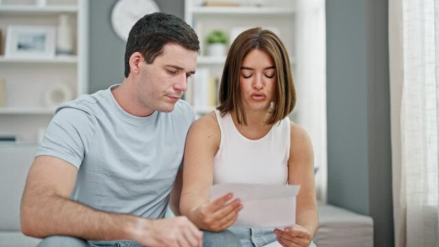 Beautiful couple reading document sitting on sofa looking upset at home