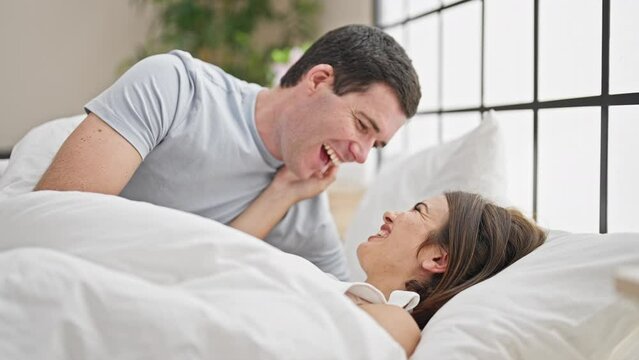 Beautiful couple smiling confident lying on bed together kissing at bedroom