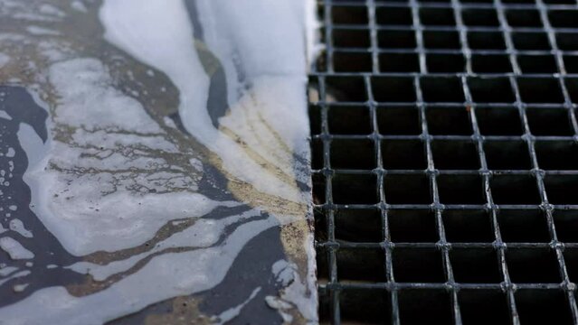 Sewerage at a car wash station. Active foam and dirty water flow down the drain after cleaning auto. Washer flushes dirt water with chemical detergent into the sewer grate. Environmental pollution.