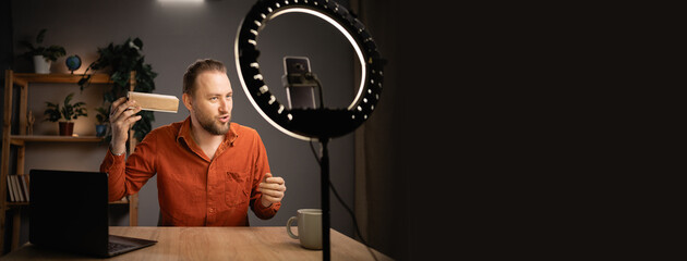 Male blogger unboxing a new gadget and reviewing a few electronic products on camera at home studio