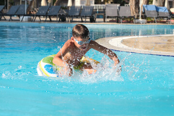 Modern vacation scene: kid in motion in a pristine resort pool with deck chairs in view