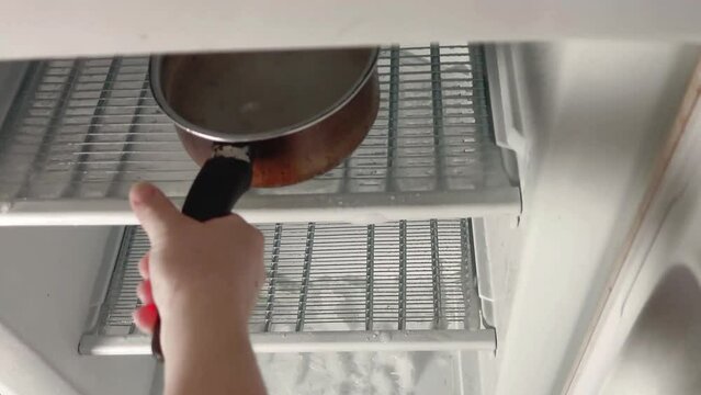 Derritiendo el hielo de un congelador con la ayuda de dos cazos con agua caliente.