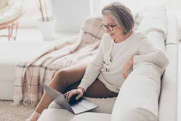 Photo of positive cheerful senior lady trader dressed white cardigan reading modern gadget indoors...