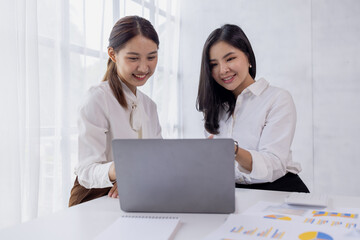 Obraz premium Two asian confident business women point to graphs and charts to analyze market data, balance sheet, account, net profit to plan new sales strategies to increase production capacity. 