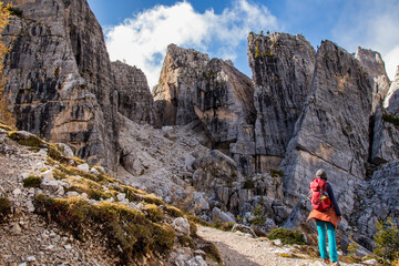 mountaineer woman with backpack hikes along a path between the huge karst walls of the Cinque Torri...