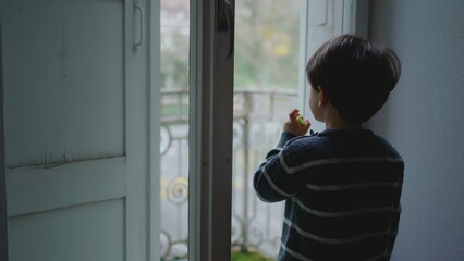 Contemplative Gaze - Young Boy Snacking by Apartment Window?Pensive Childhood Moments of Small Boy...