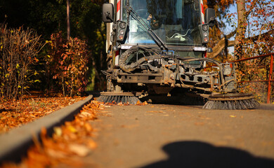 Cleaning the alleys in a park of a lot of fallen autumn leaves on the asphalt. Close up photo with a street utility car machine used to clean the public parks.