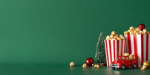 Make most of your stay-at-home holiday with our popcorn delivery concept. Side view photograph features table with popcorn, festive ornaments, miniature car, fir on green backdrop, leaving room for ad