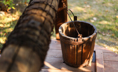 Close up photo with an old wooden bucket placed on a vintage water fountain. Old rust chain in foreground, selective focus photo. © Dragoș Asaftei
